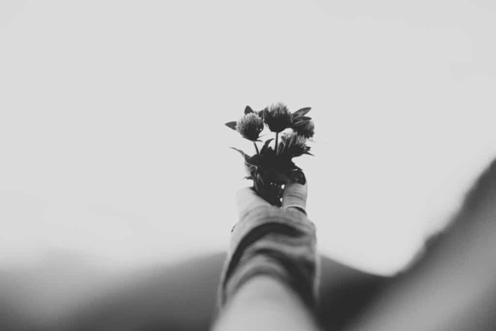 Black and white image of a hand holding a small bunch of wildflowers against a blurred outdoor background.
