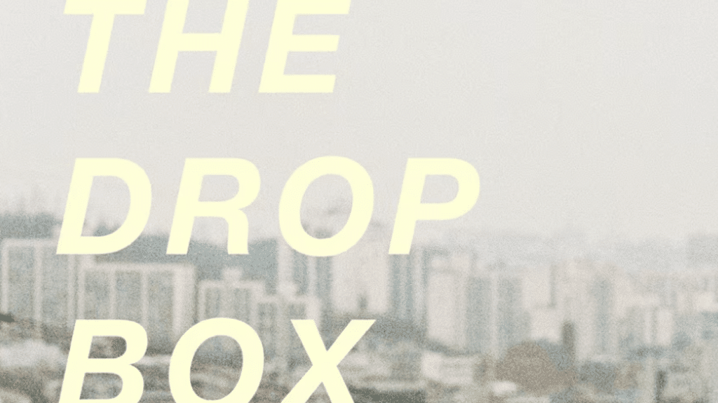 The Drop Box" in large yellow text over a blurred cityscape background.