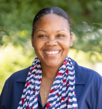 Smiling woman wearing a blue button-down shirt and a blue, white, and red striped scarf.