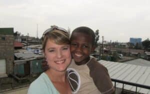 Woman and smiling boy pose together on a balcony, with rooftops and buildings visible in the background.