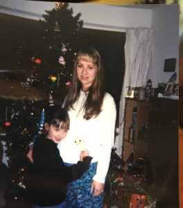 Two girls smiling in front of a decorated Christmas tree with gifts underneath in a living room.
