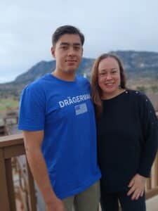 A man in a blue t-shirt with “DRÄGERMAN” text and a woman in a black sweater standing together on a wooden deck.